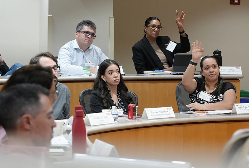 Students seated in a classroom, with several raising their hands to participate.