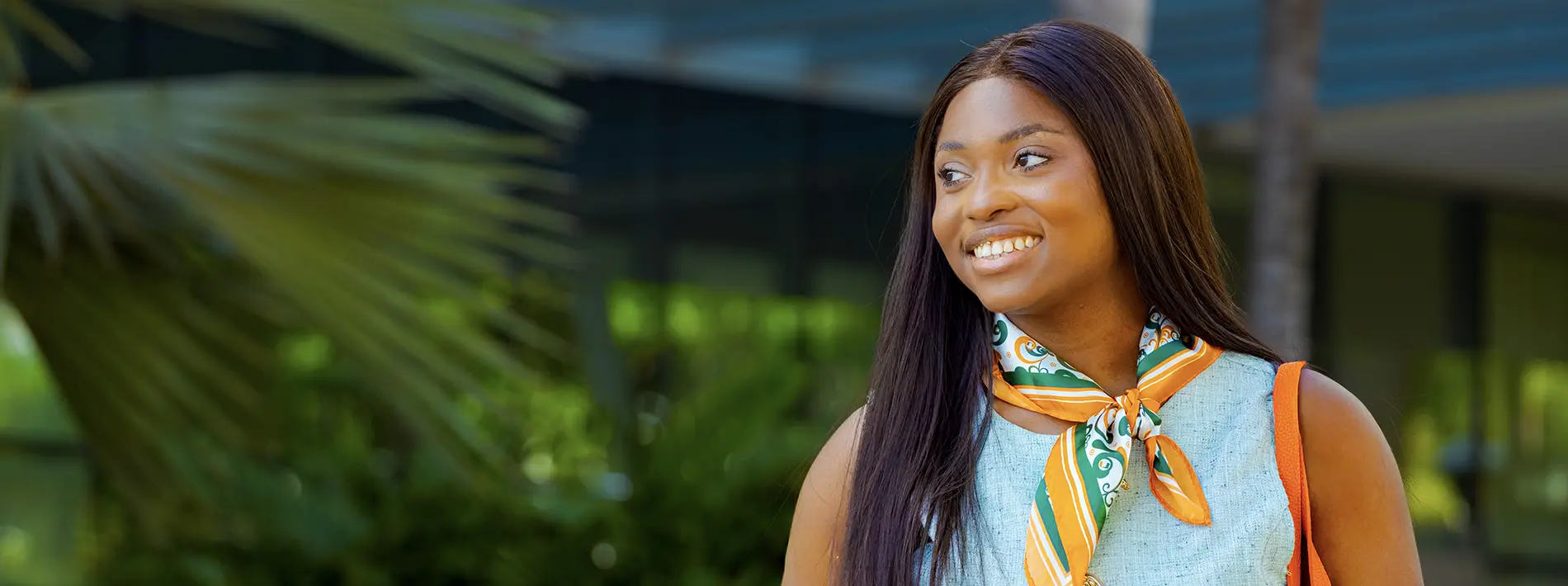 Woman with a green and orange scarf smiling while walking on campus